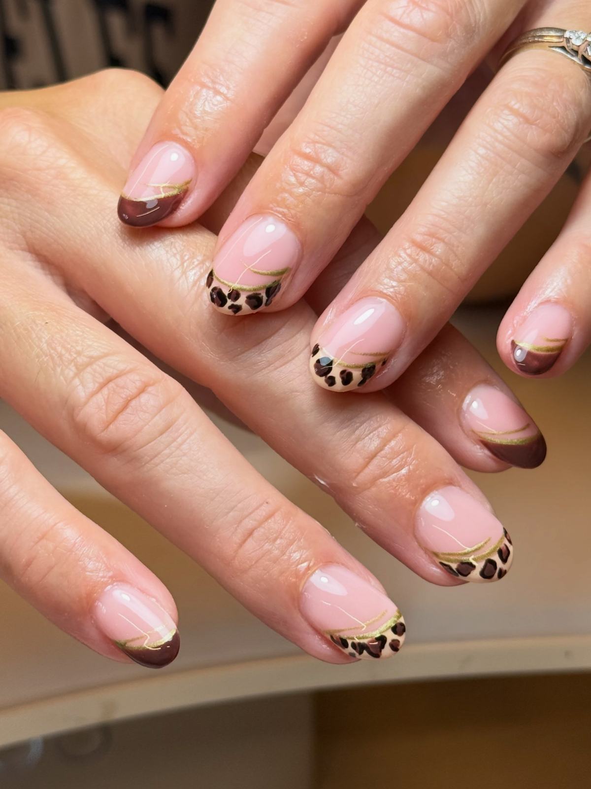 Nude pink short nails with chocolate-brown and leopard-print French tips and a gold line