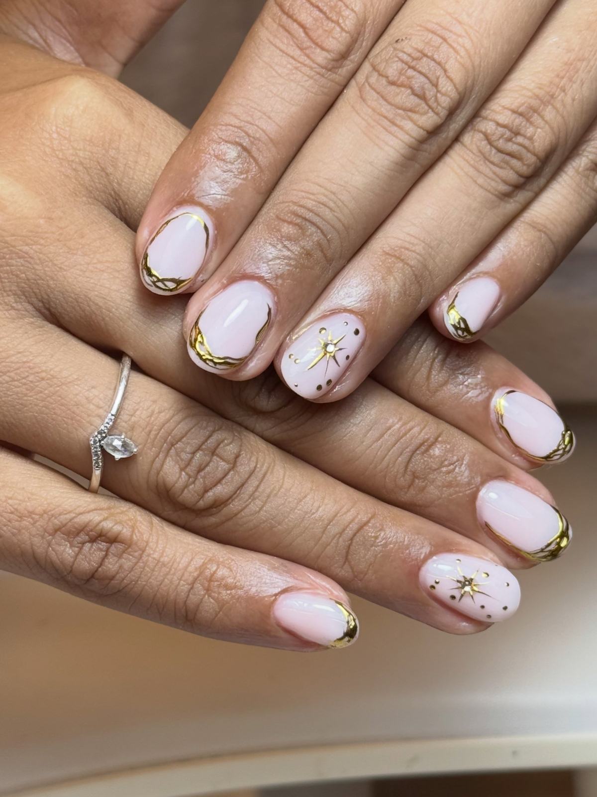 Milky-pink short nails with gold foil edges and gold starburst detail